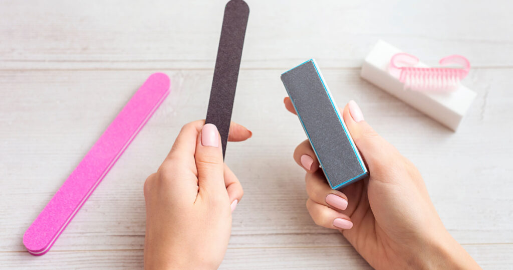 closeup of hands of a young woman filing her nails with pink manicure with a purple nail file. Woman polishing fingernails with nail file. Doing manicure with nail file. Body-care of hands
