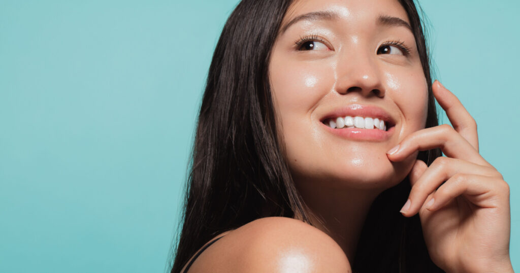 Close up of cute asian girl with glowing skin against blue background. Beautiful face of girl with fresh healthy skin. 