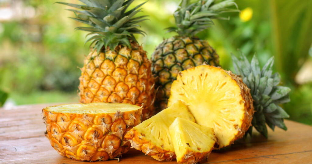Sliced and half of Pineapple(Ananas comosus) on wooden table with blurred garden background.Sweet,sour and juicy taste.Have a lot of fiber,vitamins C and minerals.Fruits or healthcare concept.

