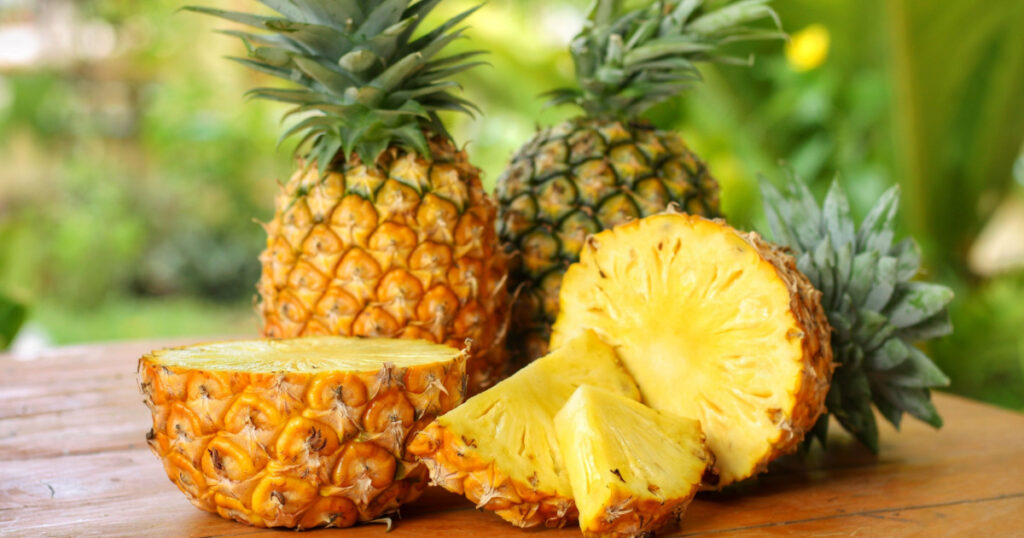 Sliced and half of Pineapple(Ananas comosus) on wooden table with blurred garden background.Sweet,sour and juicy taste.Have a lot of fiber,vitamins C and minerals.Fruits or healthcare concept. 