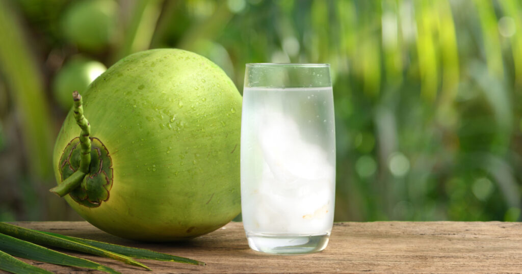 Glass of coconut juice with blurred coconut tree background.
