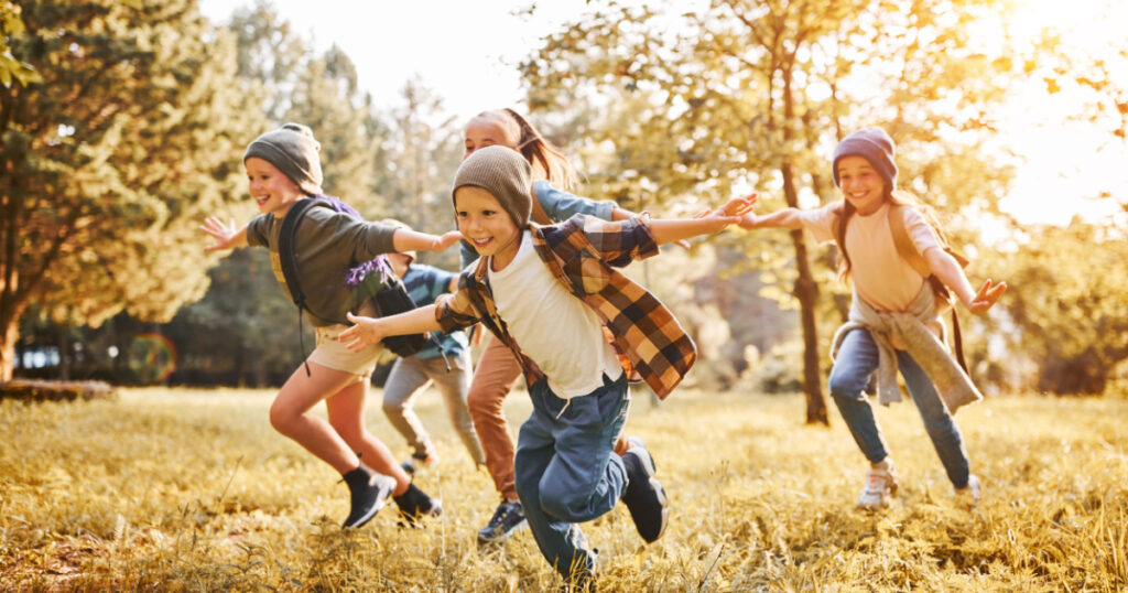 Group of happy joyful school kids with backpacks running with outstretched arms in forest on sunny spring day