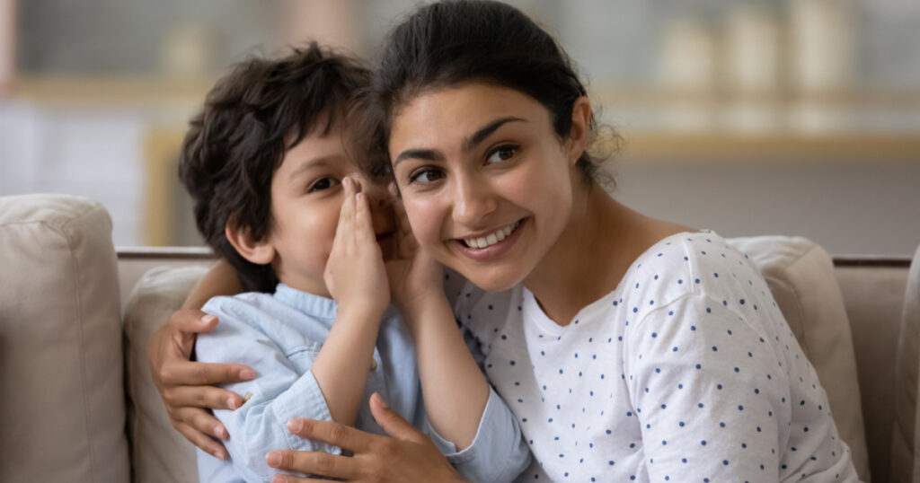 son telling secret to cheerful Indian mom, whispering in ear. Happy loving mother and kid enjoying being friendship, trust, spending leisure time