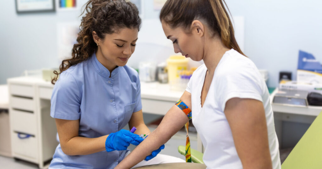 Preparation for blood test with pretty young woman by female doctor medical uniform on the table in white bright room. Nurse pierces the patient's arm vein with needle blank tube.
