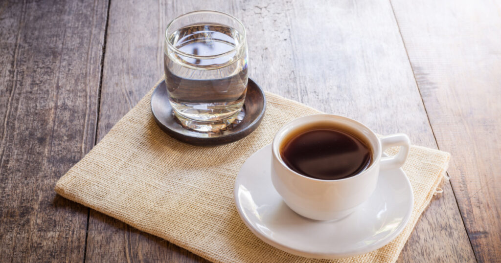 Cup of coffee on a wooden table with glass of water on the Sackcloth bags
