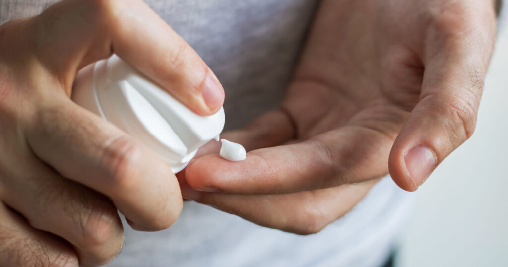 Closeup of male hands pumping out cream from white bottle on fingertip. Cream drop on index finger. Taking care of your skin - F 2.8
