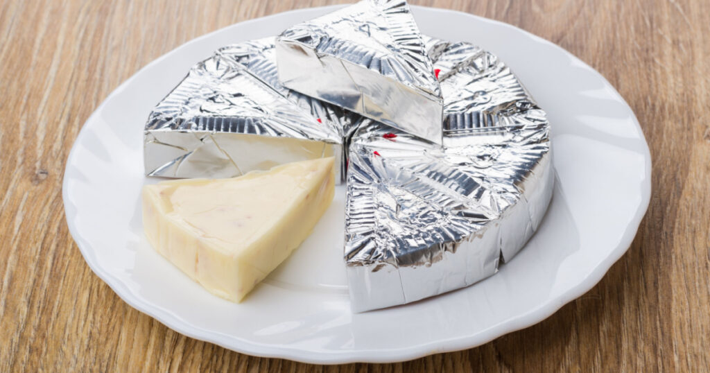 Slices of melted cheese in foil in white plate on wooden table
