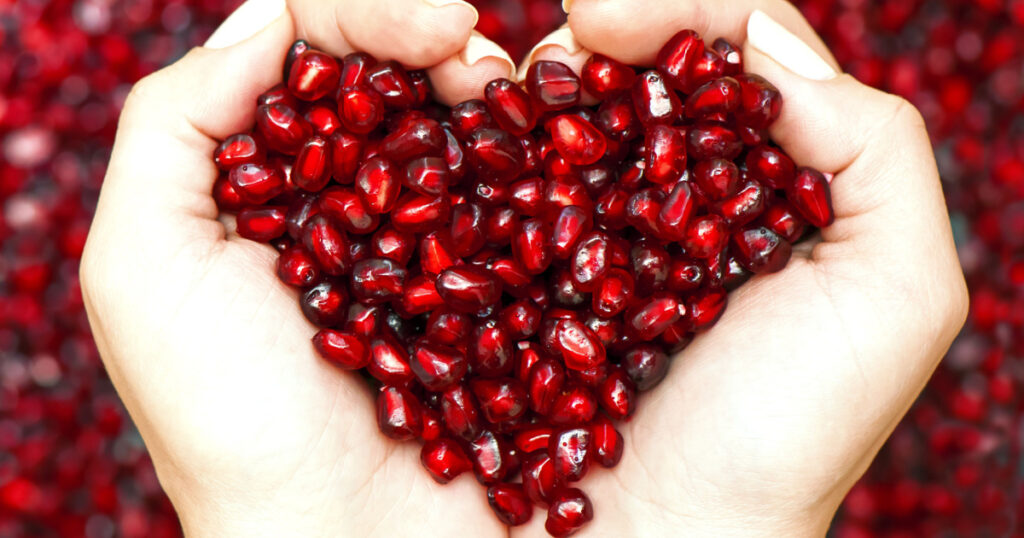 Pomegranate seeds in woman hands shaping heart symbol
