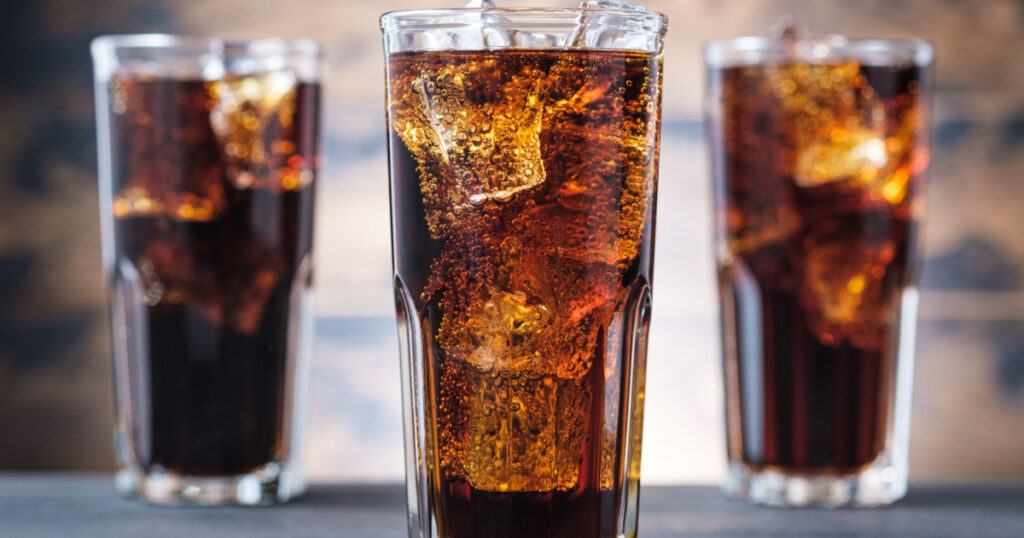 Three cola glass with ice cubes and bubbles. Cold sweet drink on wooden background
