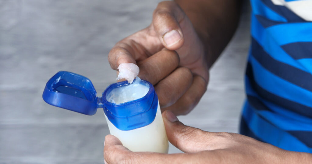 man hand use white petroleum jelly on blue background
