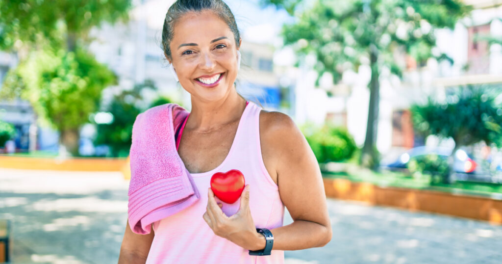 Middle age sportswoman asking for health care holding heart at the park
