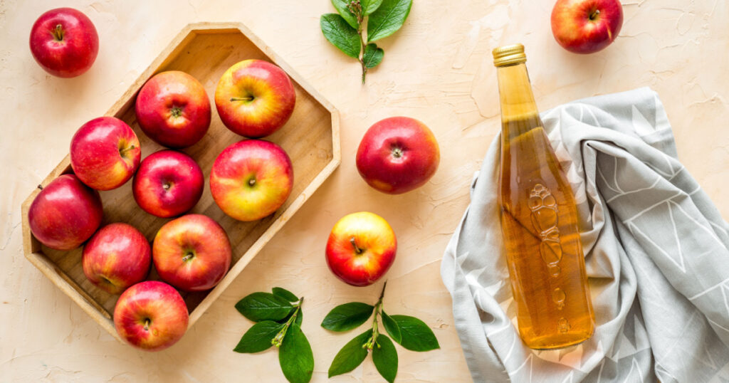 Apple cider vinegar in glass bottle and wooden tray with red apples
