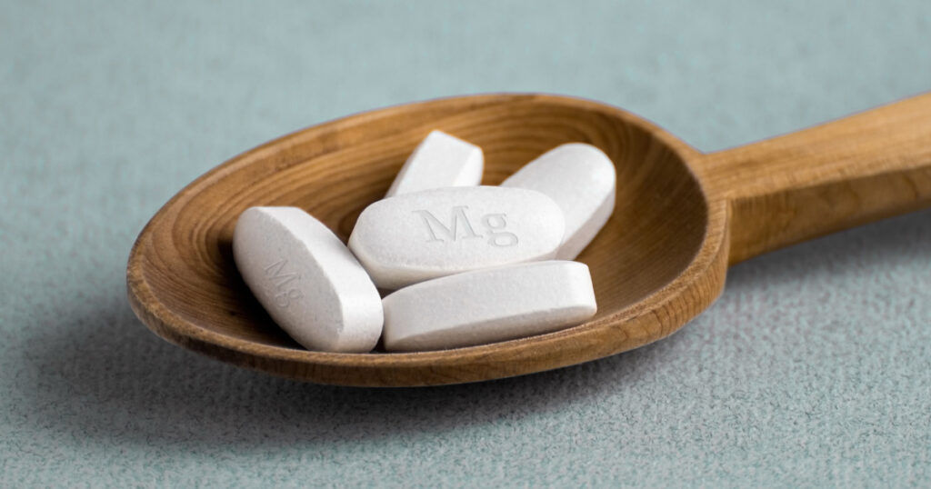 Tablets , vitamins with the abbreviation Mg ( magnesia, the macronutrient magnesium ) lying in a wooden spoon on a light background. Copy space.

