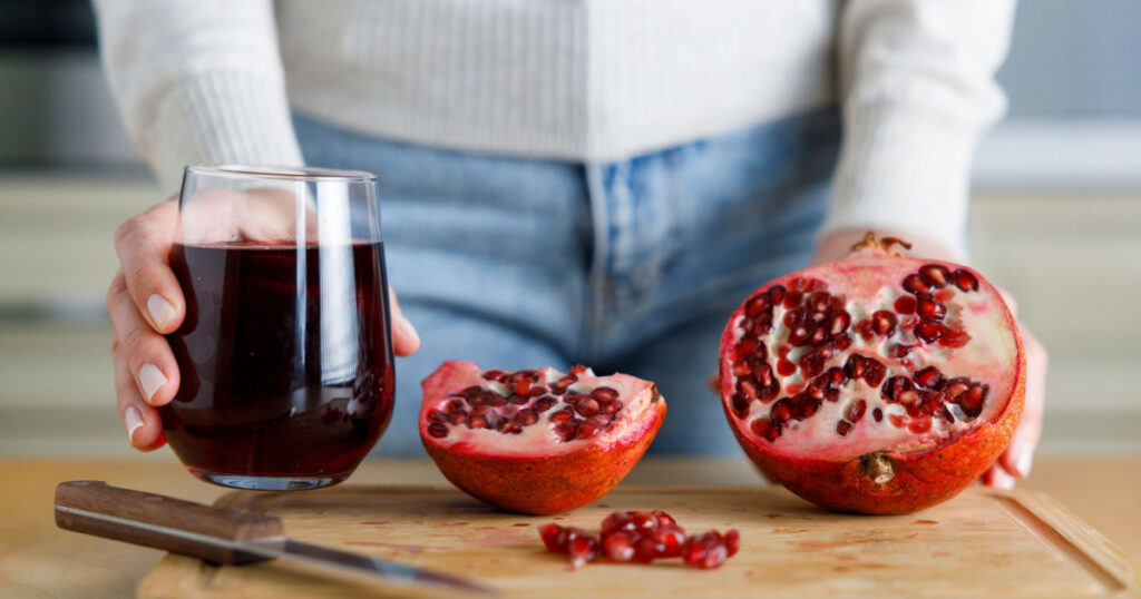 Young woman peeling a pomegranate and holding a glass of pomegranate juice
