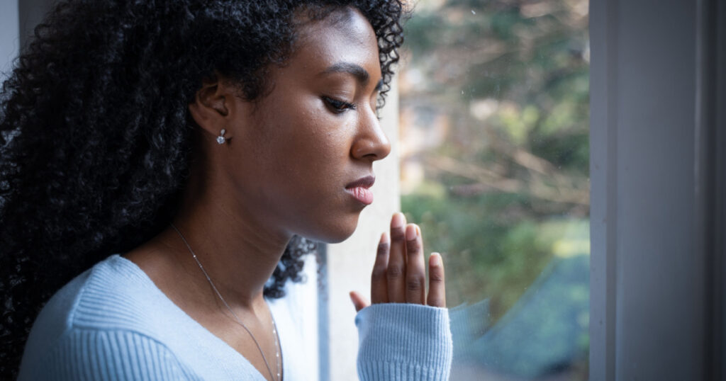 One black woman pray in front of window

