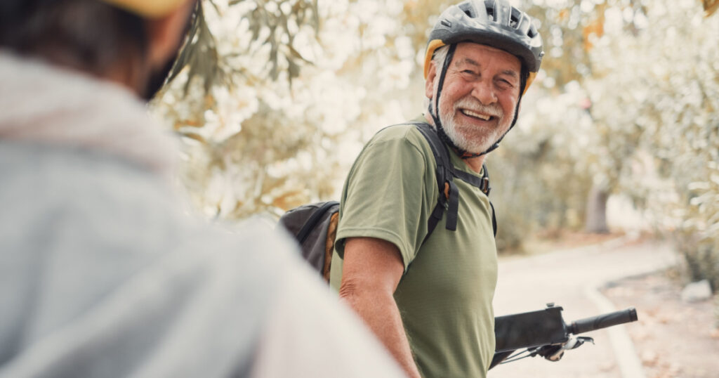 Two happy old mature people enjoying and riding bikes together to be fit and healthy outdoors. Active seniors having fun training in nature. Portrait of one old man smiling in a bike trip with wife
