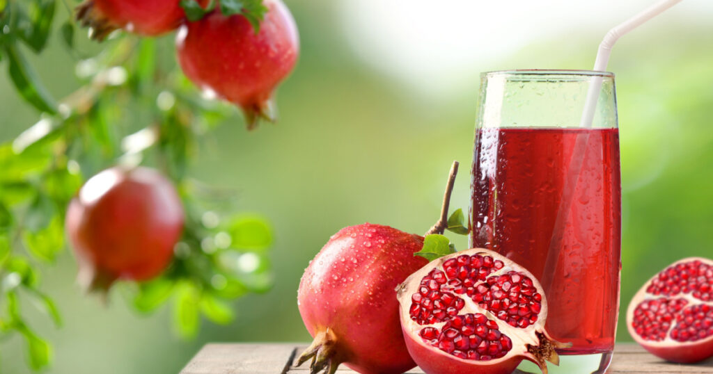 Pomegranate juice with fresh fruits on wooden table with pomegranate plant background.
