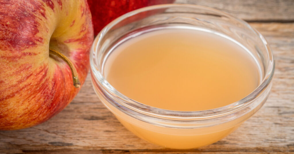 unfiltered, raw apple cider vinegar with mother - a small glass bowl with fresh red apples
