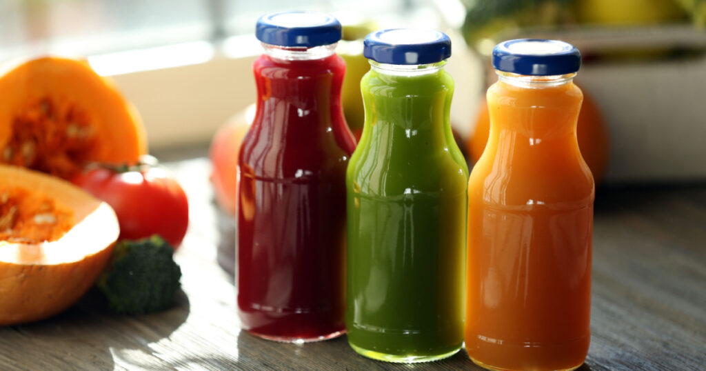 Bottles of juice with fruits and vegetables on windowsill close up
