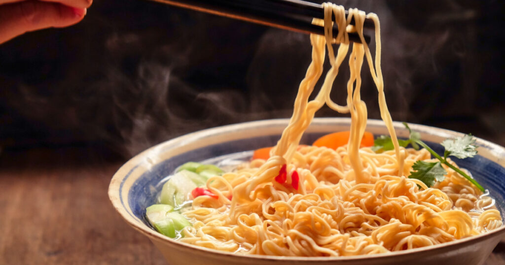 Hand uses chopsticks to pickup tasty noodles with smokes.

