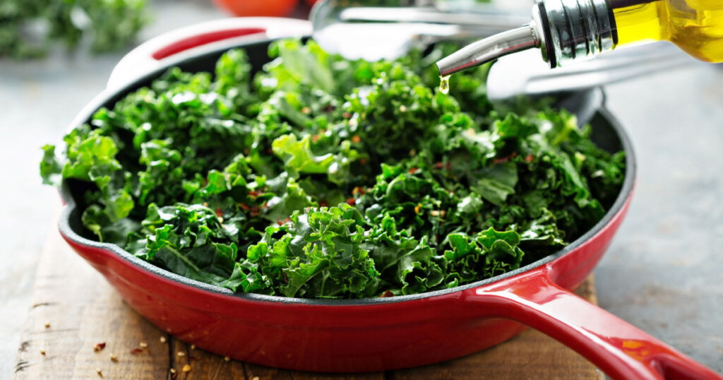 Quickly sauteed kale with chili flakes in a cast iron pan with olive oil pouring over, healthy cooking concept

