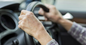 elderly hands on steering wheel in car