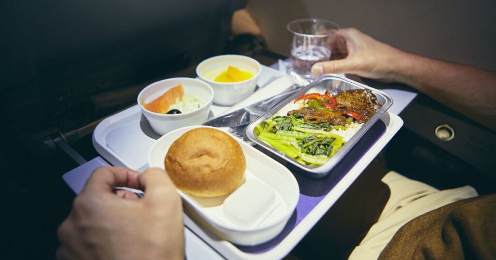 Traveling by airplane. Passenger enjoying dinner in economy class during long haul flight.
