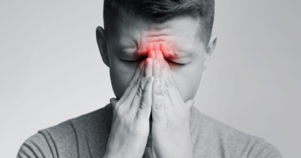 Sinus pain, sinusitis. Sad man holding his nose, black and white photo with red sore zone
