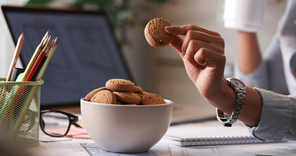 Close up of businesswoman taking cookie from a bowl while working in the office.
