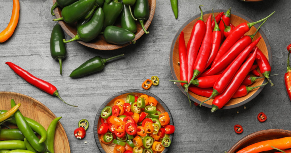 Different ripe hot chili peppers on grey table, flat lay

