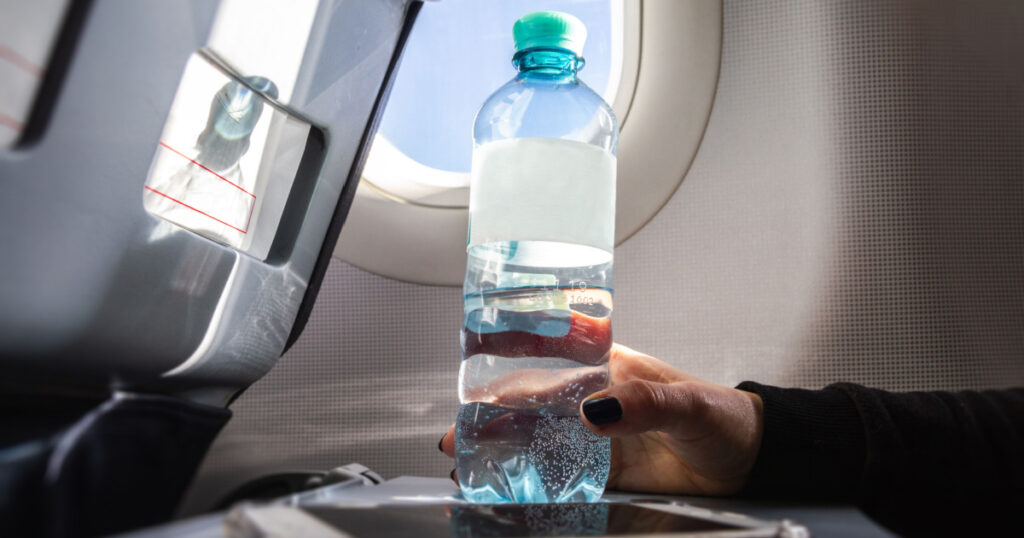Female passenger holding a bottle of water next to her phone on the airplane tray table.
