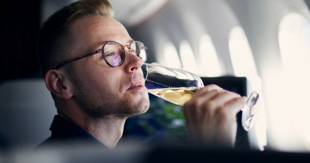 Business travel by airplane. Man looking through window and drinking champagne during flight.
