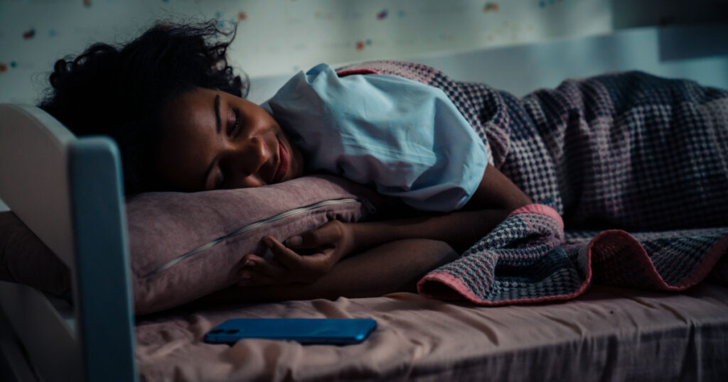 African teen girl sleeping near phone in her room at home
