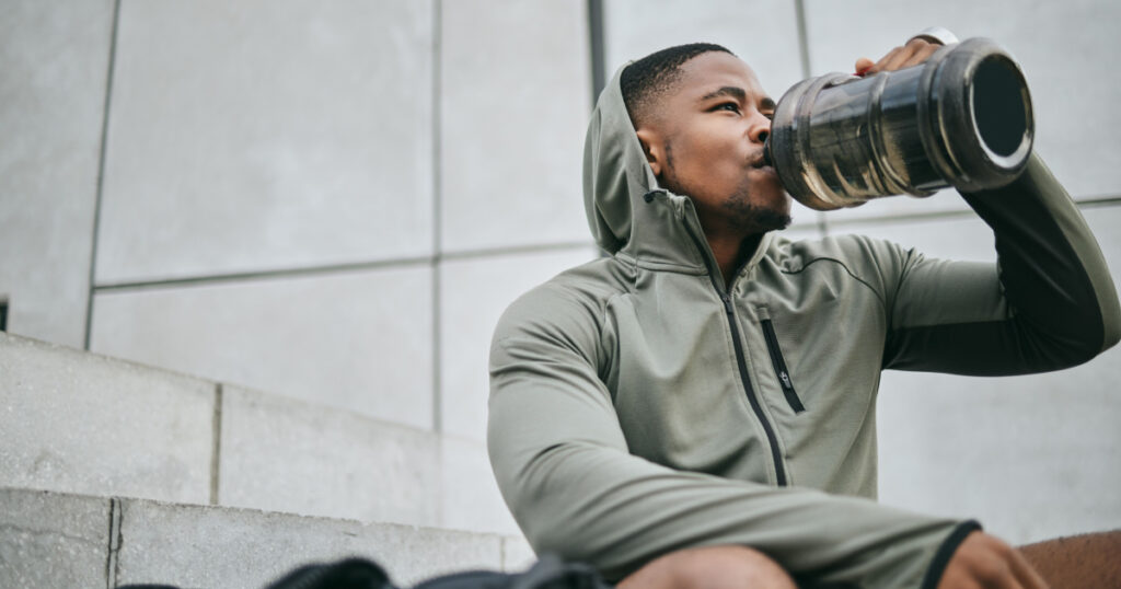 Fitness, relax or black man drinking water in training or exercise for body recovery or workout in Chicago, USA. Hydration, thirsty or tired healthy sports athlete drinks natural liquid in bottle
