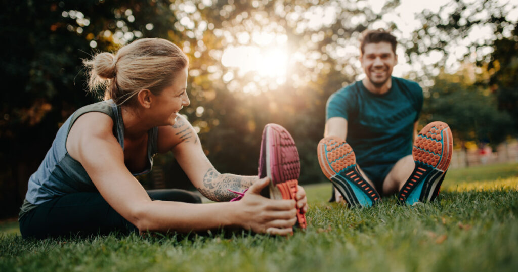 Fitness couple stretching outdoors in park. Young man and woman exercising together in morning.
