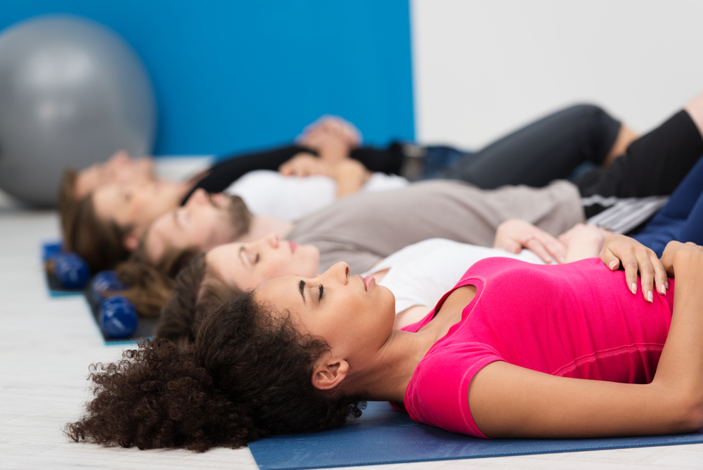 Aerobics class practicing deep breathing for relaxation lying on their backs on their mats on the floor with focus to a young African American woman in the foreground