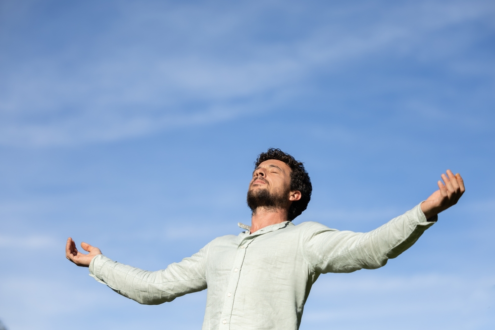 Man relaxing meditating and breathing in nature. Young man with his arms open while breathing and enjoying the sun on a summer day.
