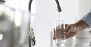 Unusual Symptom of Potentially Deadly Disease Can Be Spotted By the Amount of Water You Drink hand holding glass of water being filled at tap