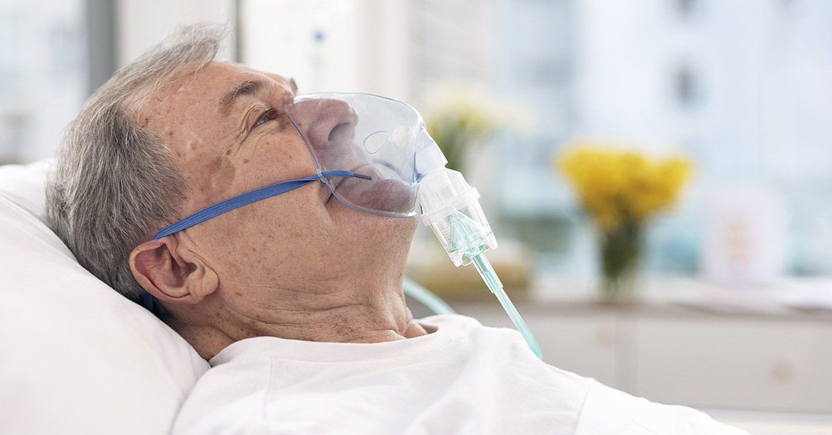 man in hospital setting in bed wearing oxygen mask