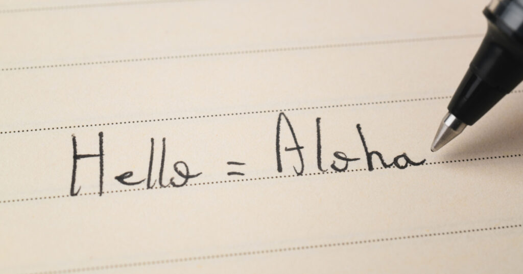 Beginner Hawaiian language learner writing Hello word Aloha for homework on a notebook macro shot