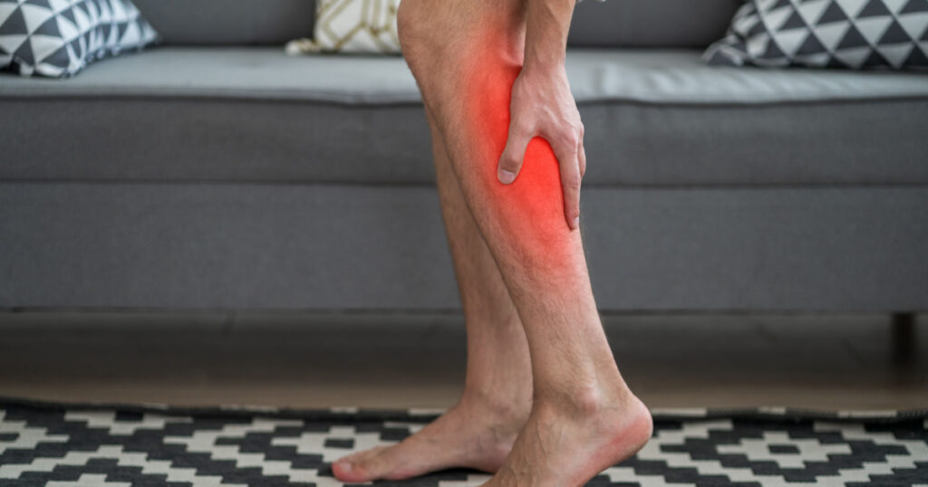 The man's calf muscle cramped, massage of male leg at home, painful area highlighted in red
