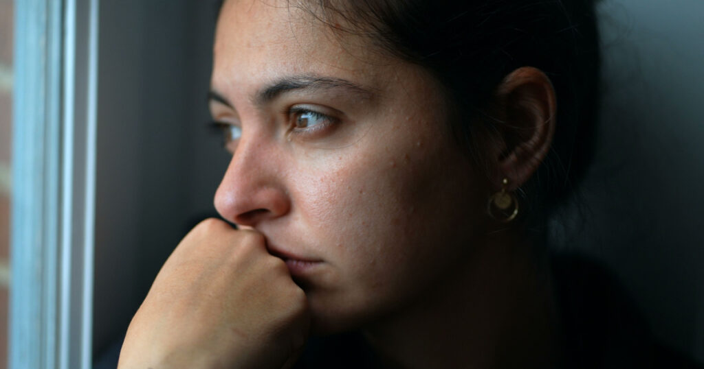 Pensive woman sitting by window looking outside. Close-up thoughtful person
