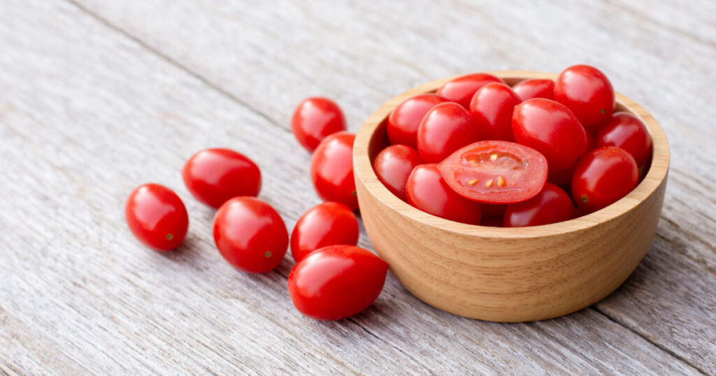 Fresh red cherry tomatoes with half sliced in wooden bowl isolated on wooden table background. Copy space.
