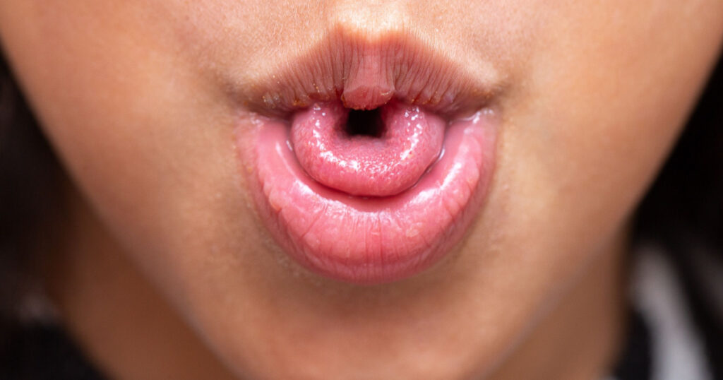 Macro of a little girl's mouth curling her tongue into a U shape, a genetic trait inherited from her parents.