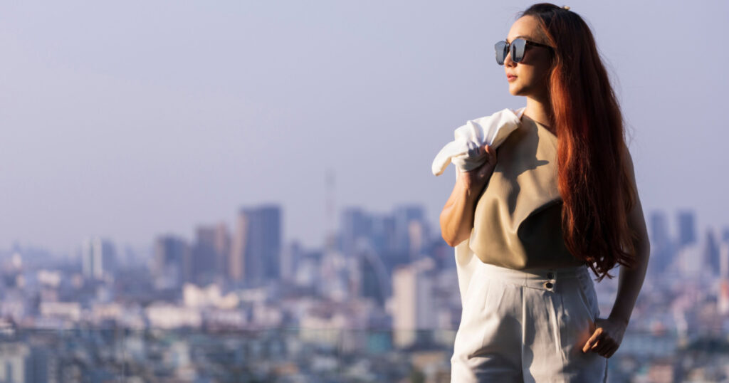 Luxury young Asian CEO woman entrepreneur standing on the rooftop looking to the sun with skyscraper and cityscape on the background with copy space