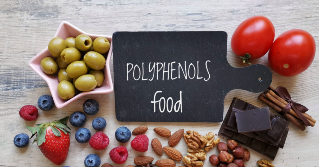 Foods rich in polyphenols with text Polyphenols Food. Natural sources of polyphenols: blueberry, raspberry, chocolate, nuts, clove, cinnamon. Polyphenols are compounds offers various health benefits.