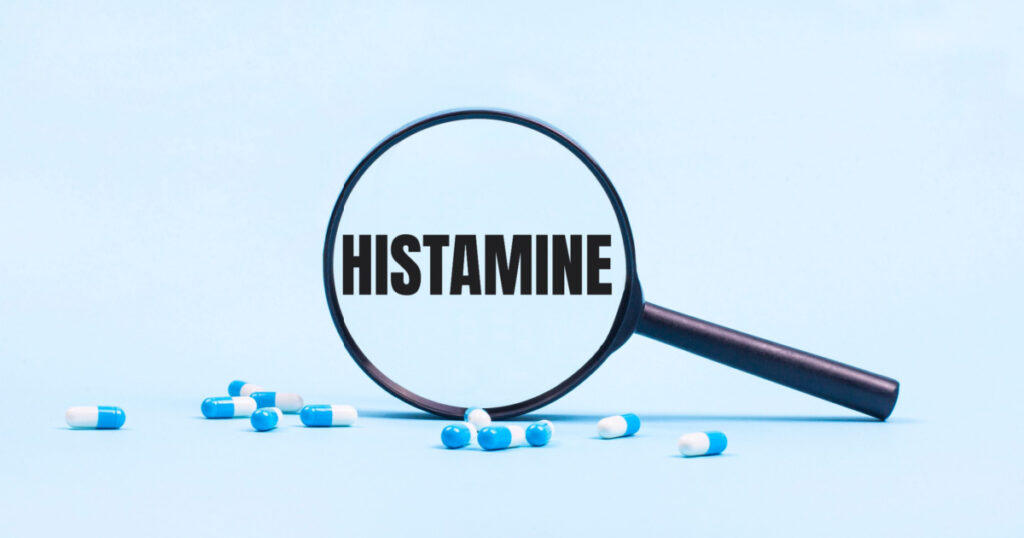 On a blue background, white and blue capsules with pills and a black magnifying glass with the text HISTAMINE. Medical concept.