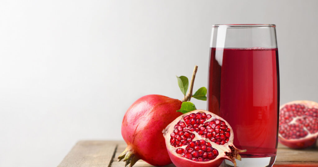 Pomegranate juice with fresh pomegranate fruits on wooden table.