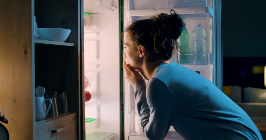 Woman looking in the fridge late at night, she is searching for a snack
