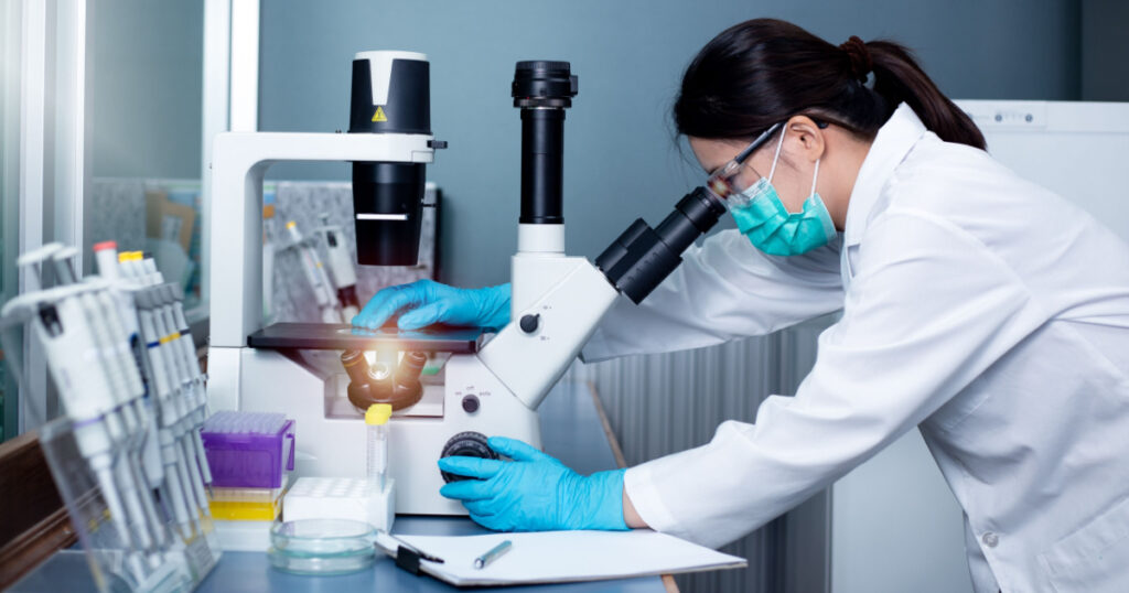 Chemical Advanced Research Laboratory, portrait of female researcher using microscope to look at culture cells on microscope slide. Research for pharmaceutical, medicine, biotechnology development.